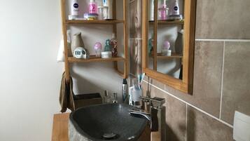 Une salle de bain avec un lavabo en pierre, des étagères contenant des articles de toilette, un miroir et un porte-serviettes.