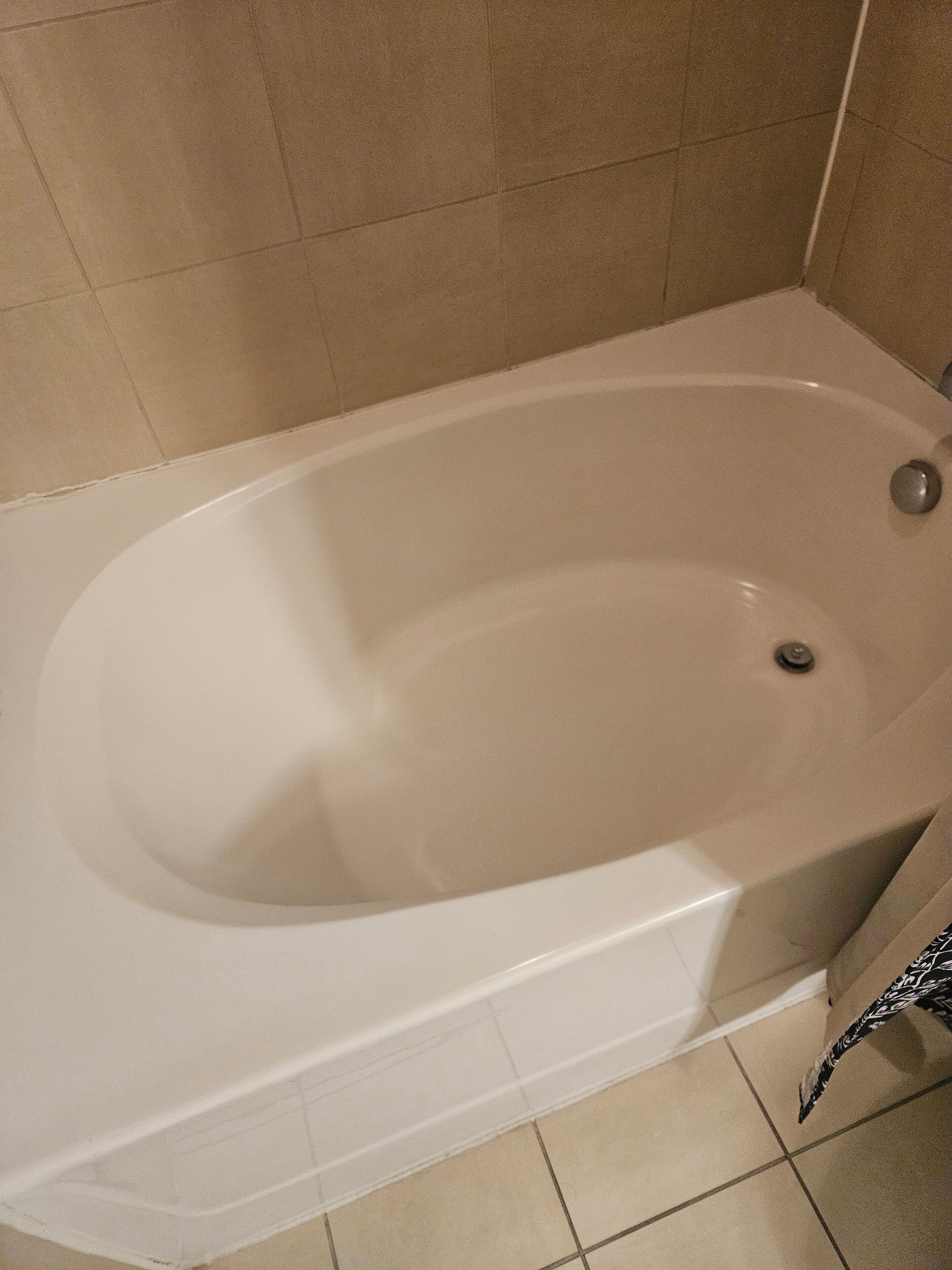 A standard bathtub in a bathroom with beige tiles on the walls and floor.