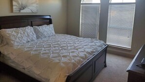 Une chambre à coucher avec un lit, une table de chevet et deux fenêtres équipées de stores.