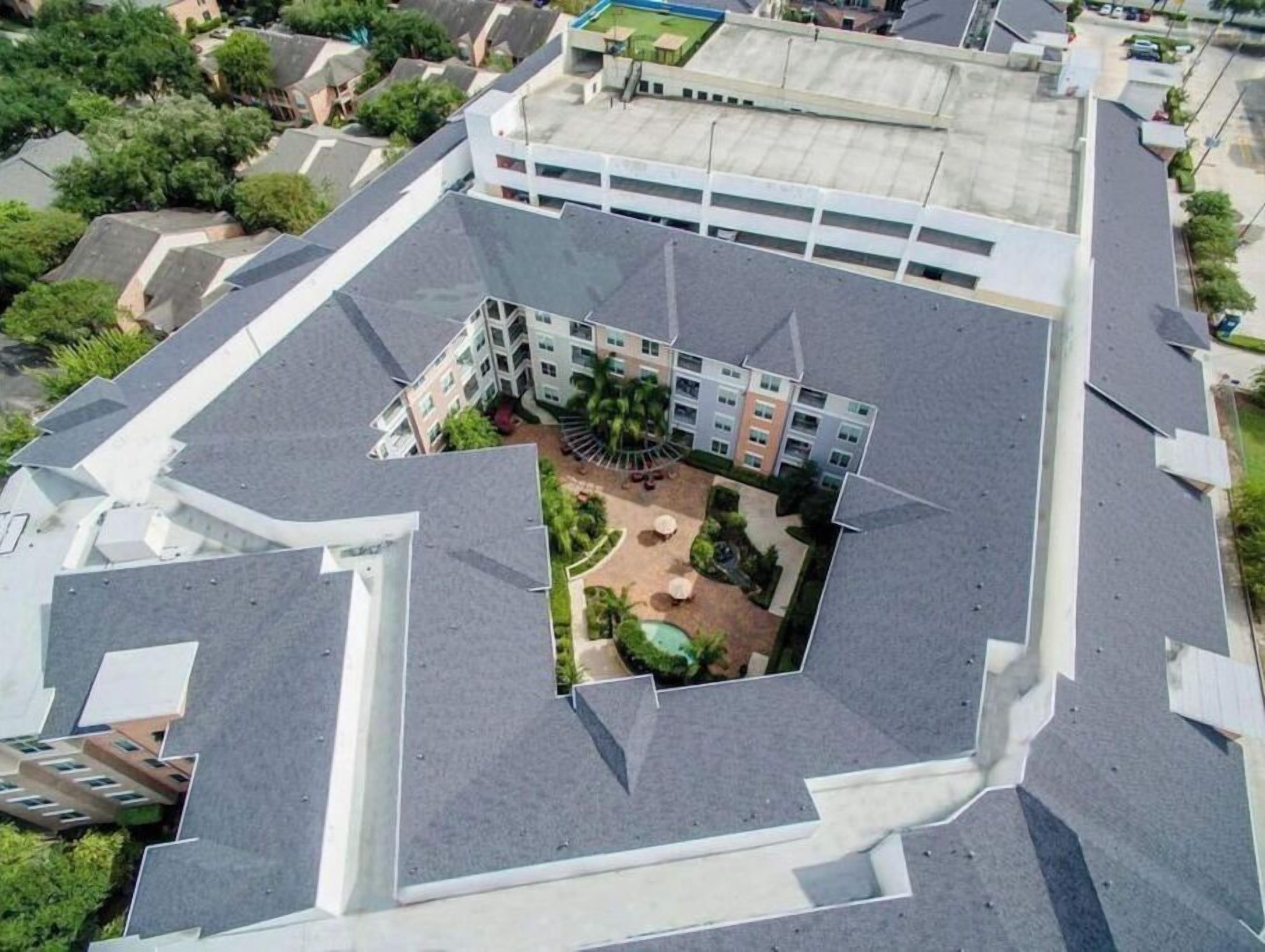 Un edificio de varios pisos con un patio central, rodeado de balcones y una piscina al fondo.