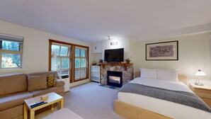 Una habitación acogedora con sofá, cama, chimenea, televisión y ventana con vistas a árboles.