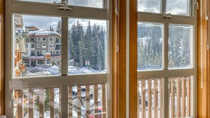 Habitación de hotel con amplios ventanales que ofrecen vistas a una montaña nevada y un edificio de techo rojo.