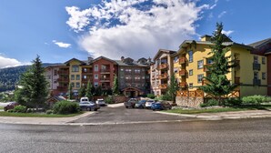 Un hotel de varios pisos con balcones, estacionamiento y montañas al fondo.