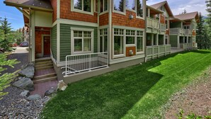Ein zweistöckiges Haus mit grünen und braunen Fassade, einer Veranda und einem gepflegten Rasen.