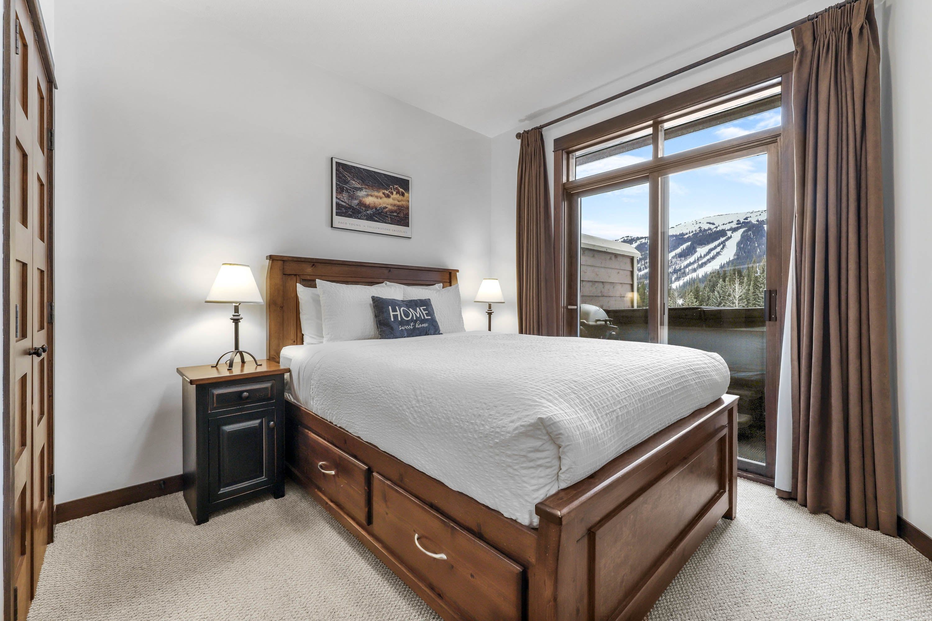 A hotel room with a large bed, two bedside tables with lamps, a headboard, a window with curtains, and a picture on the wall.