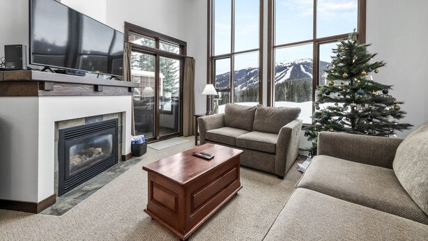 A living room with a fireplace, a television, a Christmas tree, and a large window offering a mountain view.