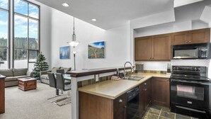 A modern kitchen with a large island, dark wood cabinets, a black microwave, and a dishwasher.