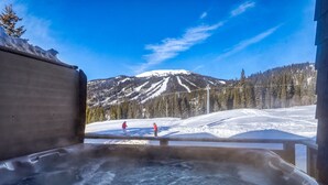A hot tub with a view of a snowy mountain and skiers.