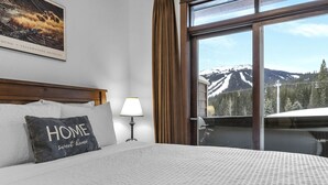 A hotel room with a bed, a pillow with "HOME sweet home" text, a lamp, a window with a mountain view, and a framed picture on the wall.
