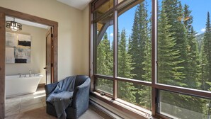 Ein Badezimmer mit einer Badewanne, einem großen Fenster mit Blick auf einen Wald und einem Sessel am Fenster.