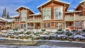 A multi-story lodge with large windows and a stone facade, featuring a stone retaining wall and snow-covered landscaping. - Pet Friendly, Ski In/Ski Out, 3 Bedroom Condo in Stone's Throw! (Sun Peaks)
