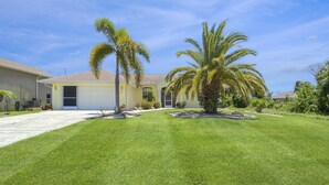Il s’agit d’une propriété résidentielle dotée d’une pelouse bien entretenue, de deux palmiers et d’une maison avec un garage et un patio couvert.