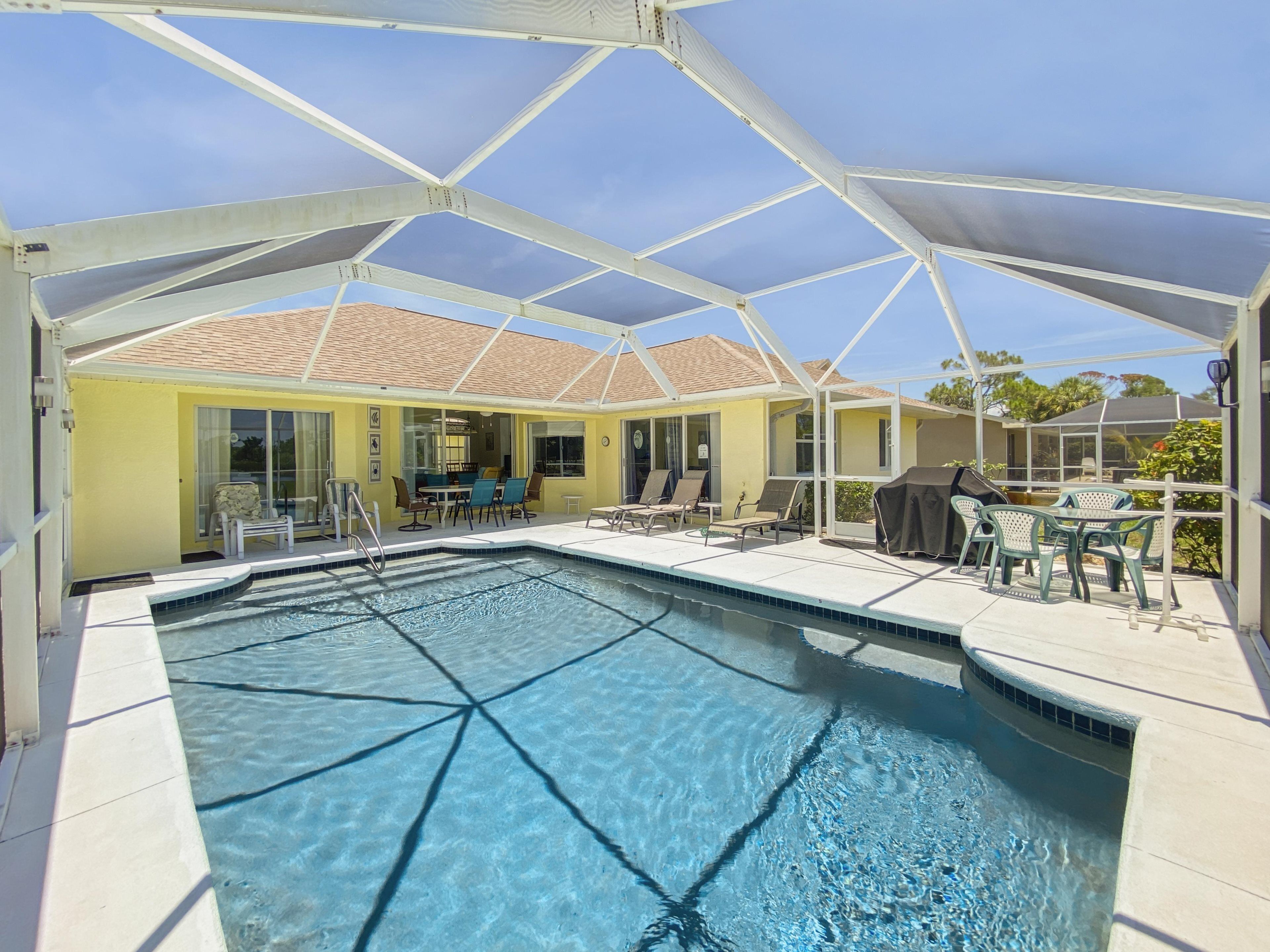 A covered swimming pool with clear blue water, surrounded by lounge chairs and a patio area.