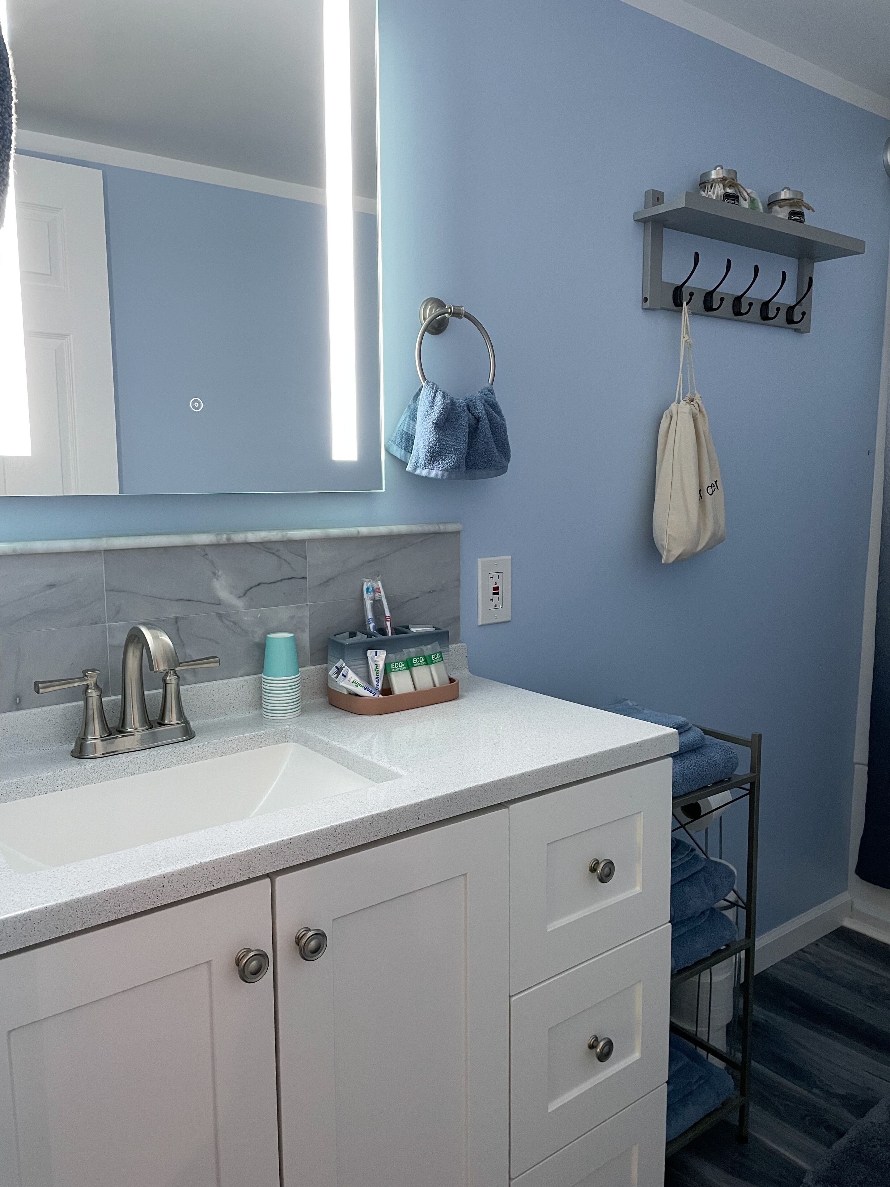 A bathroom with a white vanity, a sink with a modern faucet, a towel rack with a blue towel, and a shelf with toiletries.