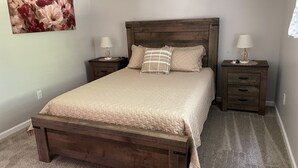 A bedroom with a wooden bed, two nightstands with lamps, a large floral painting on the wall, and a carpeted floor. - Luxurious, private, contemporary 1BR apartment in Ithaca NY!  (Ithaca)