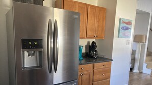 A stainless steel refrigerator with a water dispenser, wooden cabinets, a coffee maker, and a tiled floor. - Just steps to the beach, bar, and playground park! (Surf City)