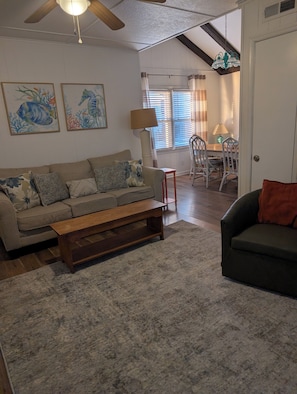 A living room with a sofa, a bench, a dining area with chairs, and artwork on the wall. - Just steps to the beach, bar, and playground park! (Surf City)