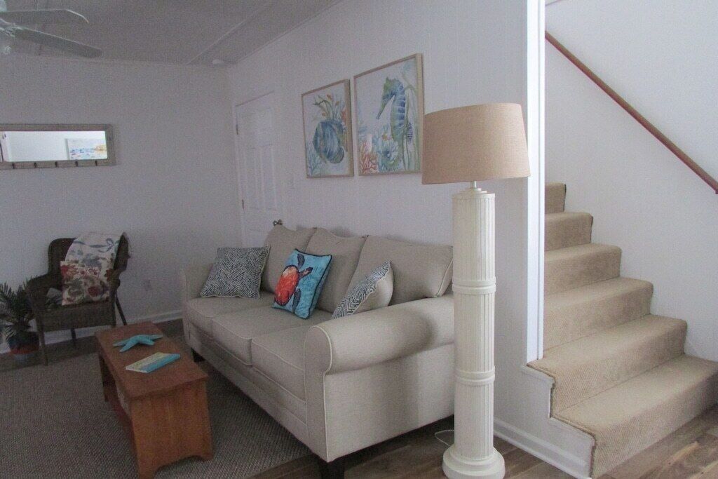 A living room with a beige sofa, a wooden coffee table, and a lamp. There is a staircase to the right.