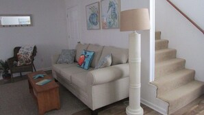 A living room with a beige sofa, a wooden coffee table, and a lamp. There is a staircase to the right. - Just steps to the beach, bar, and playground park! (Surf City)