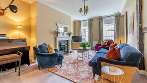 Ein Wohnzimmer mit einem Klavier, Sofas, einem Kamin und einem Fernseher.