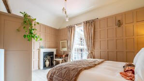 Ein Schlafzimmer mit einem großen Bett, einer hängenden Pflanze, einem Kamin und einem Fenster mit Vorhängen.