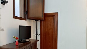 Una habitación con un armario de madera, un televisor, un espejo, una puerta y un pequeño estante con plantas.