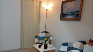 Un pequeño comedor con una mesa, dos sillas, un florero con flores, una lámpara y un cuadro en la pared.