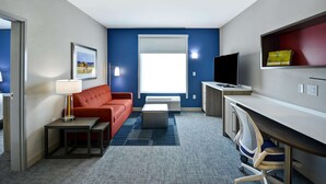 Ett hotellrum med en röd soffa, ett litet bord med en lampa, en tv på ett stativ, ett skrivbord med en stol och ett stort fönster.