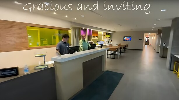 En hotellobby med modern design, en receptionsdisk och en sittgrupp med bord och stolar.