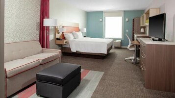 Quarto de hotel com cama, sofá, escrivaninha, televisão e banheiro.