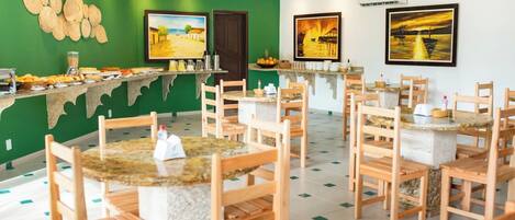 Un restaurant avec des chaises et des tables en bois, des murs verts et des œuvres d’art.