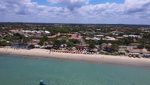 Vue aérienne d’une ville côtière avec une plage de sable, de nombreux parasols et un petit bateau sur l’eau.