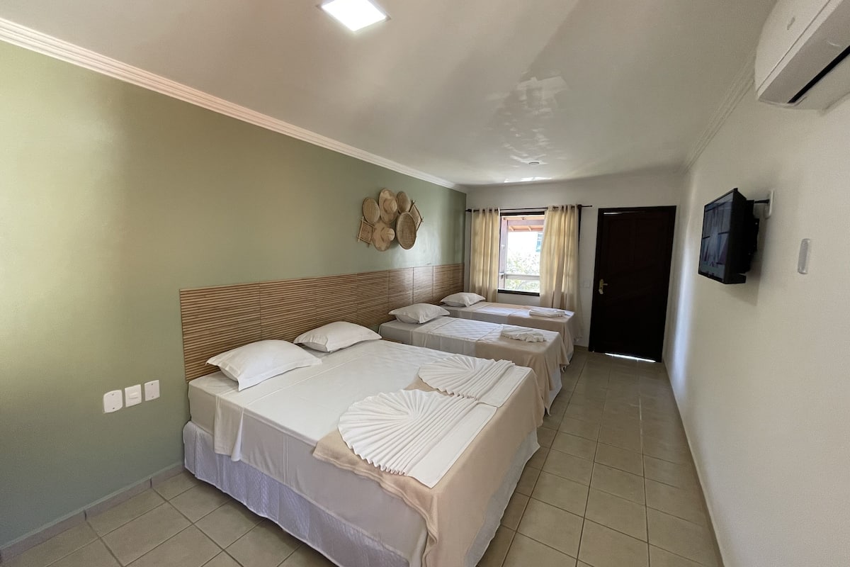 A hotel room with three beds, a television, and a window with curtains.