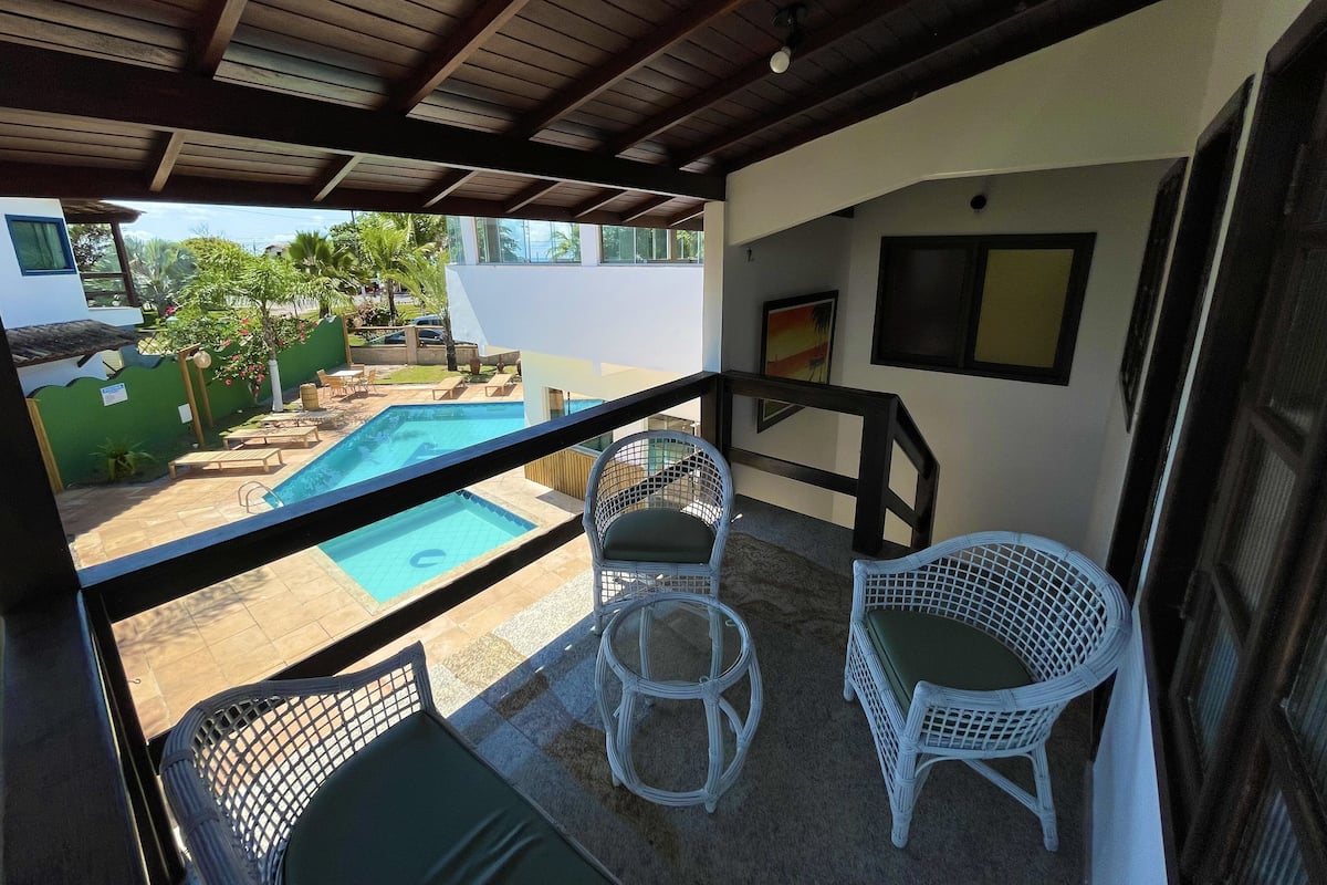A covered outdoor area with a pool, white wicker furniture, and a view of the surrounding landscape.