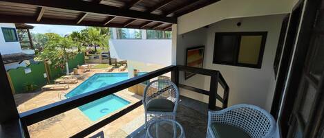 Un espacio al aire libre cubierto con piscina, muebles de mimbre blanco y vistas del paisaje circundante.