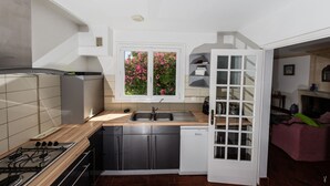 Una cocina moderna con estufa a gas, pileta de acero inoxidable y una ventana con flores rosas.