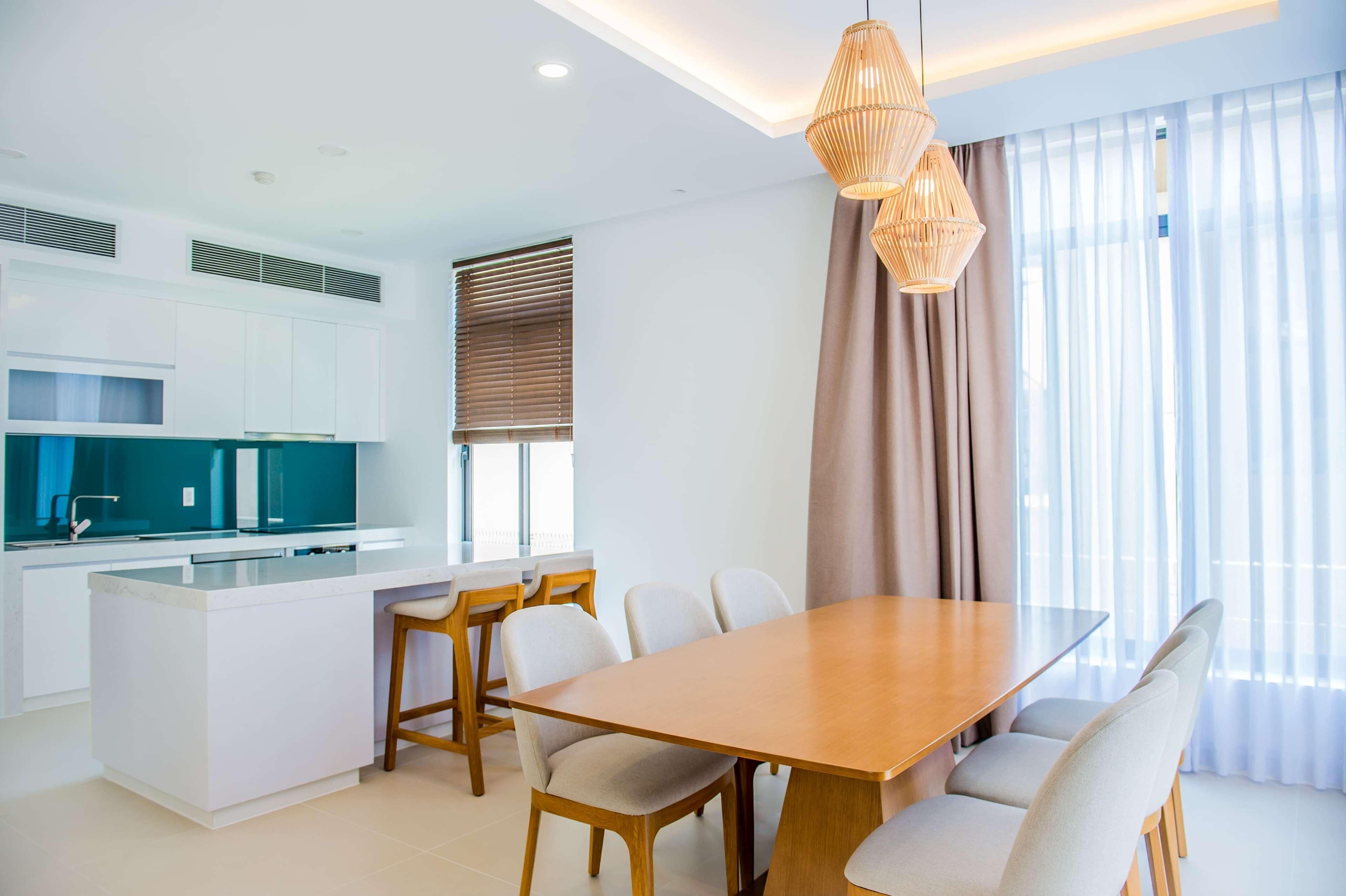 Una cocina moderna con armarios blancos, una isla central y un comedor con mesa y sillas de madera.