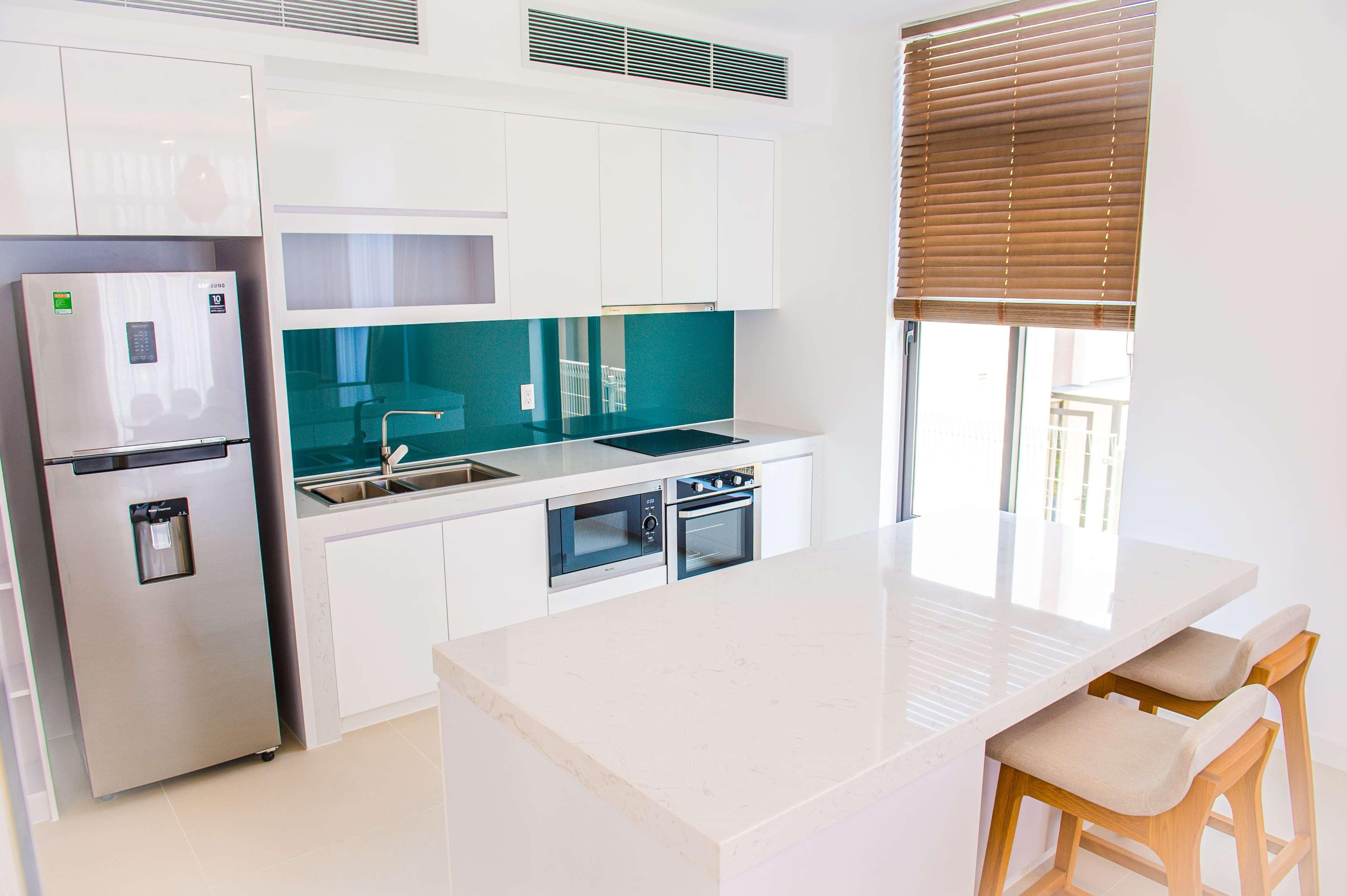 Una cocina moderna con armarios blancos, un refrigerador de acero inoxidable, un horno doble y un salpicadero color turquesa.