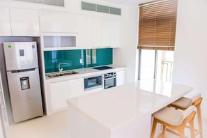 Une cuisine moderne avec des armoires blanches, un réfrigérateur en acier inoxydable, un four double et un pare-feu de couleur turquoise.