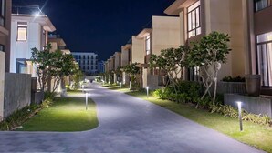 A nighttime view of a modern residential building with a paved walkway, illuminated windows, and well-maintained greenery. - Wyndham Garden Cam Ranh Resort (Cam Ranh)