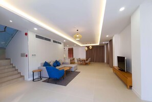 A modern living room with a sofa, coffee table, TV stand, and dining area. - Wyndham Garden Cam Ranh Resort (Cam Ranh)