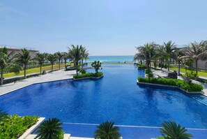 A large, clear blue pool with palm trees and a view of the ocean. - Wyndham Garden Cam Ranh Resort (Cam Ranh)