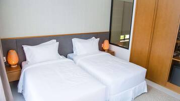 A hotel room with two single beds, a wooden wardrobe, a nightstand with a lamp, and a large mirror.