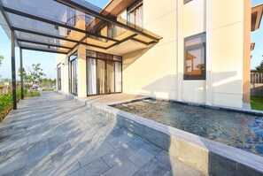 A modern building with a covered outdoor area, a swimming pool, and a paved walkway.