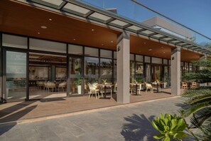 A modern building with large glass windows, outdoor seating area with tables and chairs, and a wooden deck. - Wyndham Garden Cam Ranh Resort (Cam Ranh)
