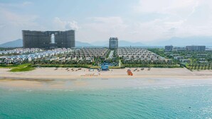 A coastal resort with a sandy beach, a pool, and a large building complex in the background. - Wyndham Garden Cam Ranh Resort (Cam Ranh)