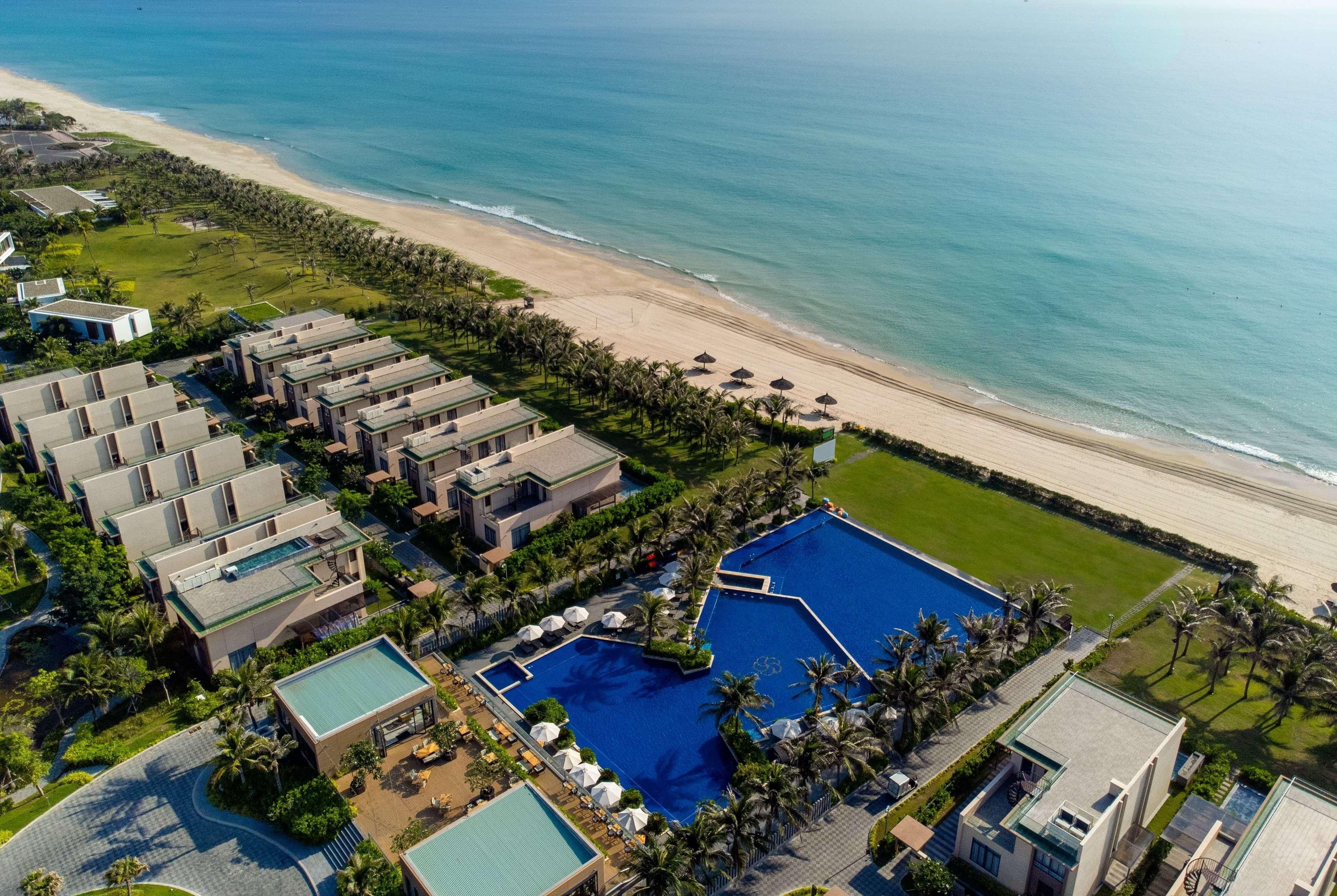 Vista aérea de un resort con varias edificaciones, una piscina grande y una playa.