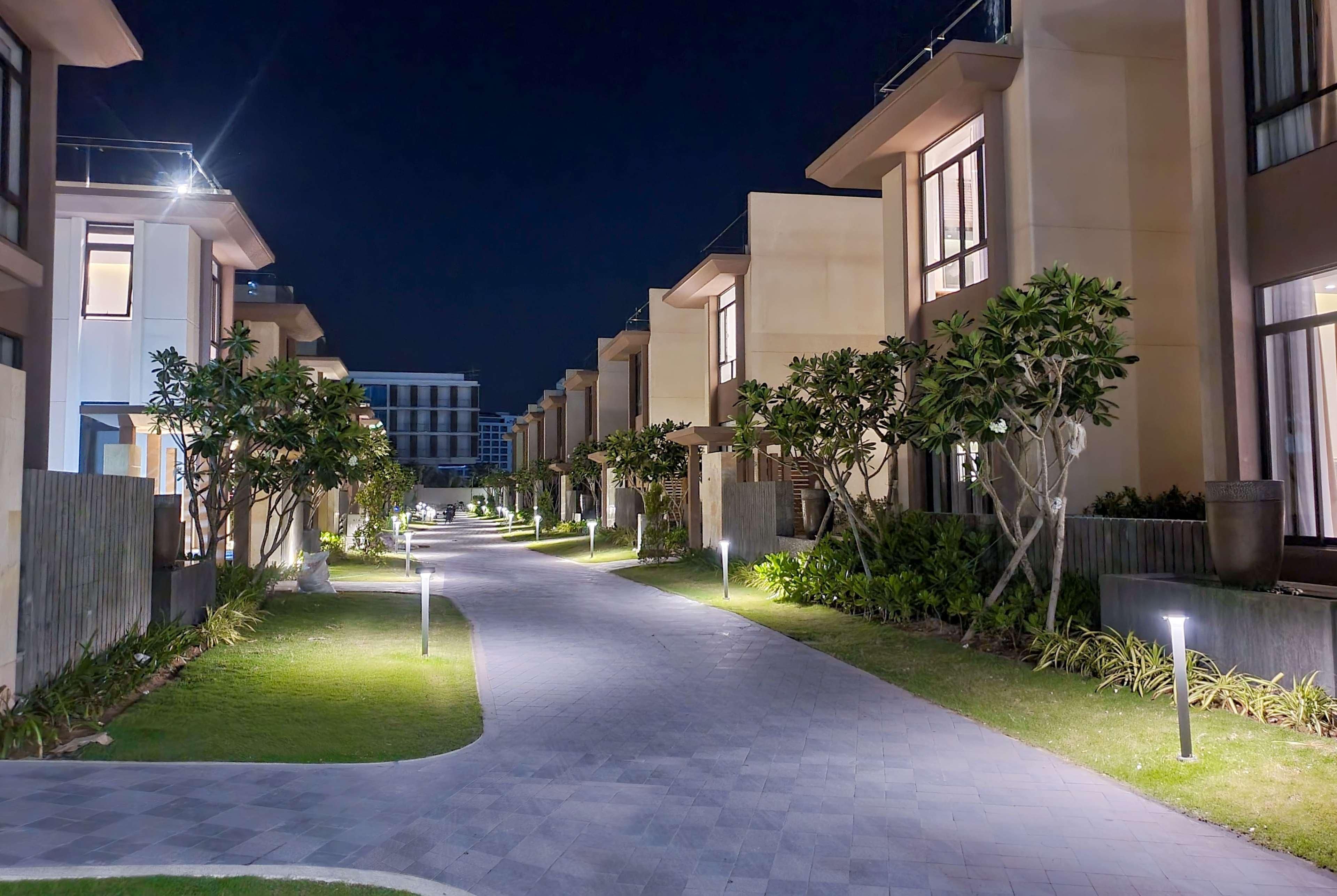 Vista nocturna de un moderno edificio residencial con un paseo empedrado, ventanas iluminadas y jardines bien cuidados.