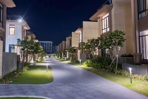 A nighttime view of a modern residential building with a paved walkway, illuminated windows, and well-maintained greenery. - Wyndham Garden Cam Ranh Resort (Cam Ranh)