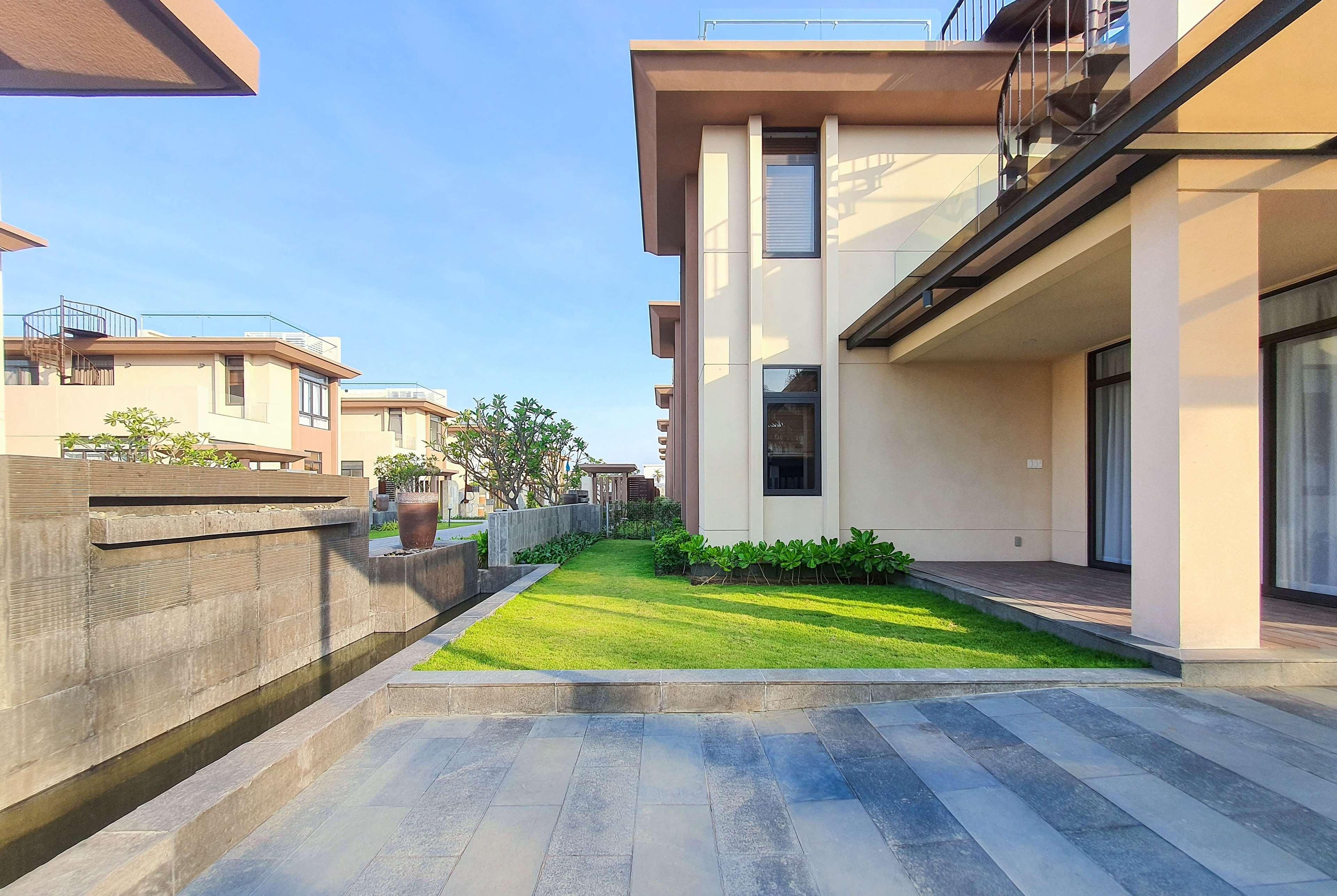 Un edificio residencial moderno con techo plano, un pequeño jardín y un sendero pavimentado.